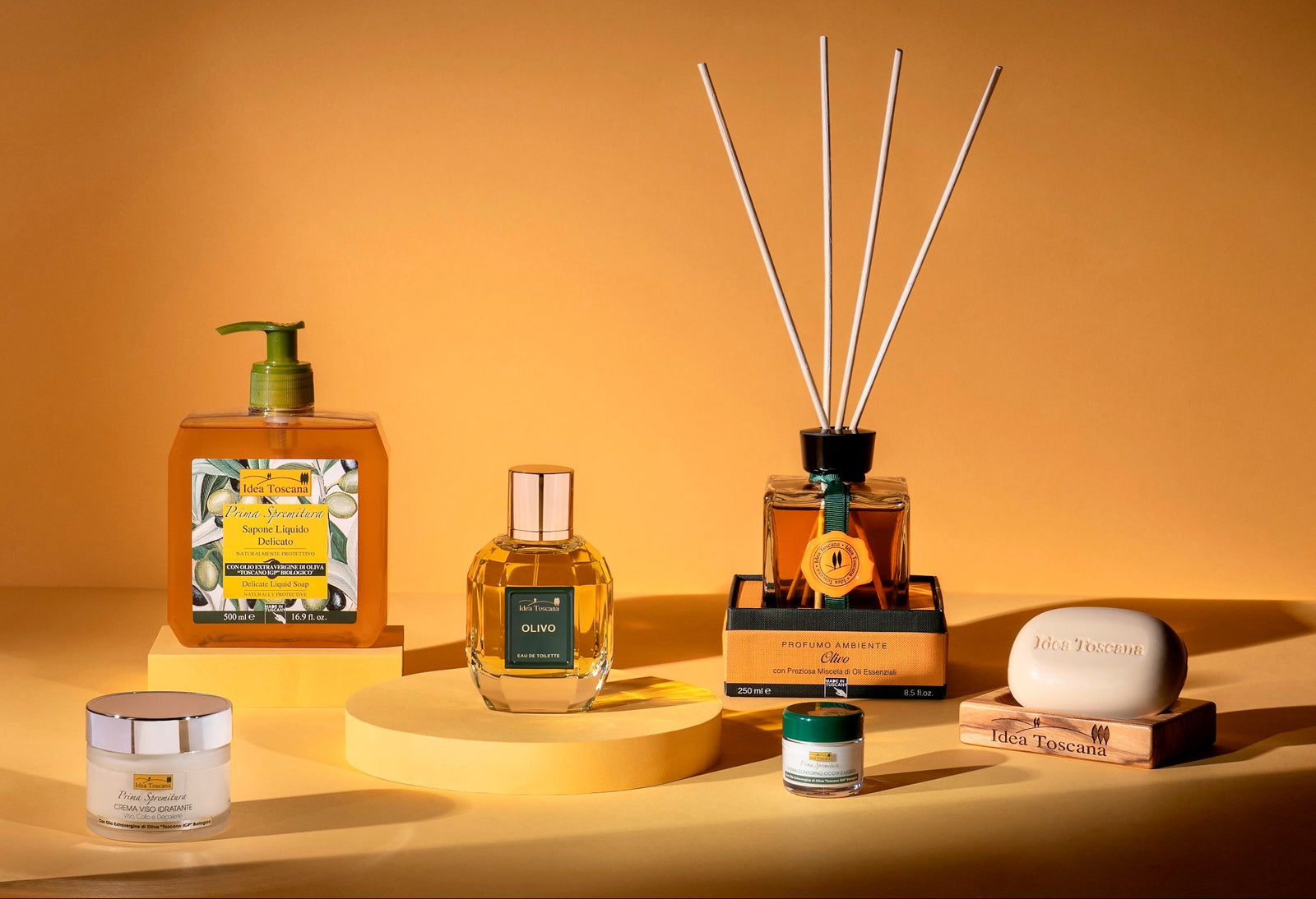 Collection of beauty products including a diffuser, bottles, and jars on a warm yellow background